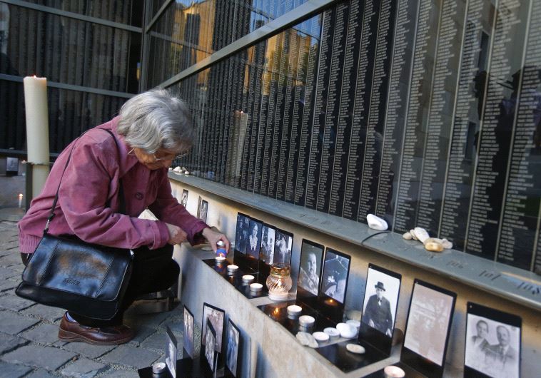 A woman lights a candle in front of a wall containing the names of victims, during the Holocaust memorial day at Budapest's Holocaust Memorial Centre April 16, 2013