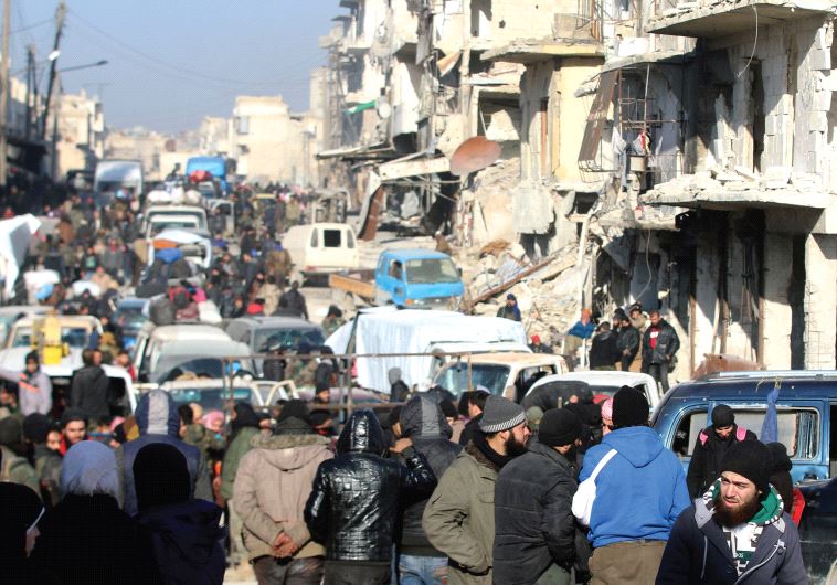 SYRIAN REBELS and civilians wait near damaged buildings to be evacuated from a rebel-held sector of eastern Aleppo.