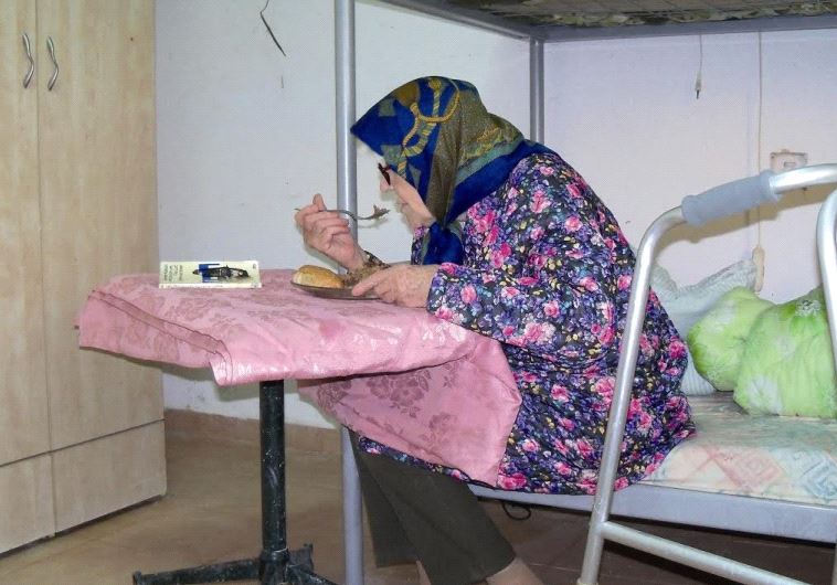 An elderly Holocaust survivor enjoys a warm meal thanks to the Association for Immediate Help for Holocaust Survivors