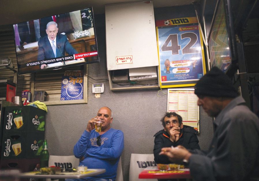 PEOPLE SIT at a kiosk in Ashkelon as a television broadcasts Prime Minister Benjamin Netanyahu’s speech to the US Congress on March 3, 2015.