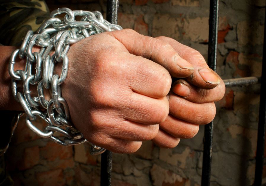 Man with hands tied up with chains behind the bars (illustrative)