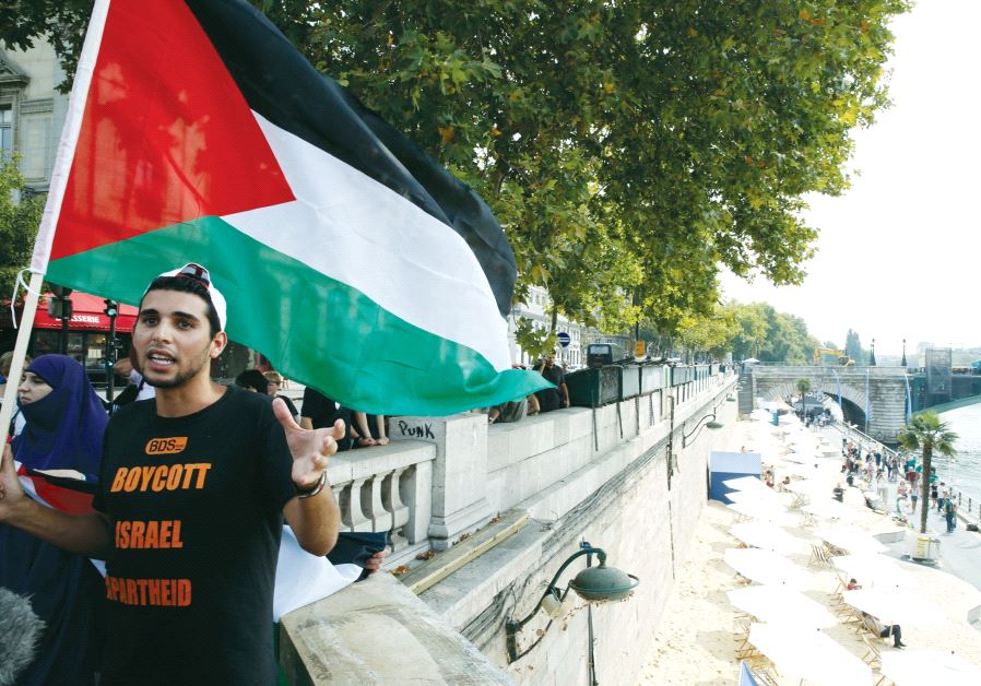A man wearing a T-shirt with the message ‘Boycott Israel Apartheid’ holds a Palestinian flag during a protest event, in Paris in 2015