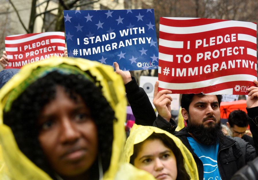 People hold up signs before marching to Trump Tower during a protest organized by the New York Immigration Coalition against then President-elect Donald Trump, December 18, 2016