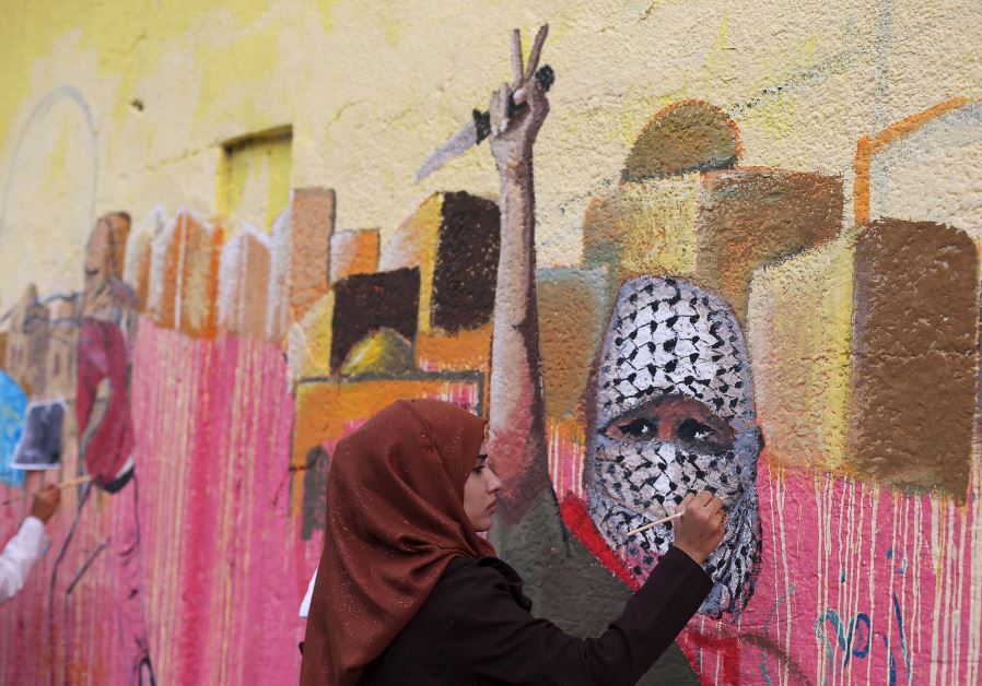 A Palestinian woman paints a mural, depicting a masked Palestinian holding a knife, in support of Palestinians committing stabbing attacks against Israelis, in Rafah in the southern Gaza Strip