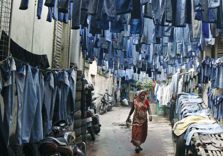 A woman walks through an alley where used pairs of jeans are hung to dry before they are sold in a secondhand clothes market in Kolkata, India, 2015