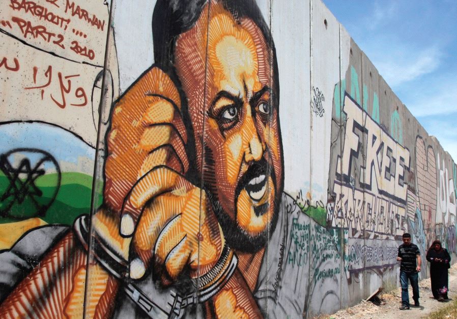 PALESTINIANS WALK past graffiti depicting jailed Fatah leader Marwan Barghouti, currently serving five life terms for terrorism, on a section of the security wall on the road to Ramallah.