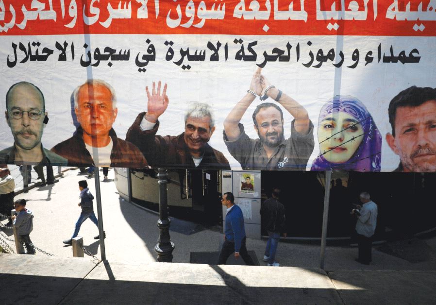 People in Ramallah walk past a poster depicting Palestinian prisoners held in Israeli jails