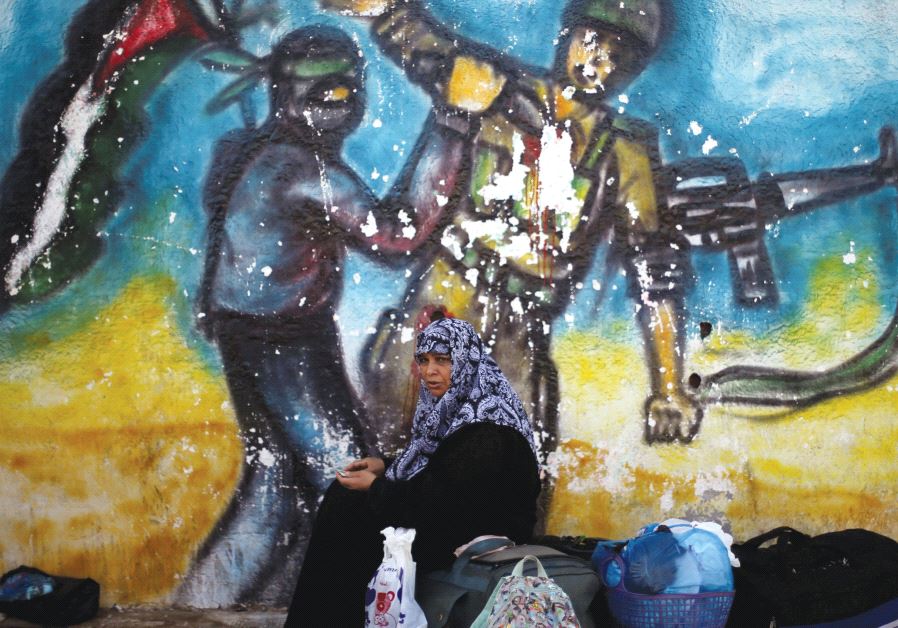 A WOMAN sits in front of a mural as she waits for a travel permit to cross into Egypt through the Rafah Crossing last year