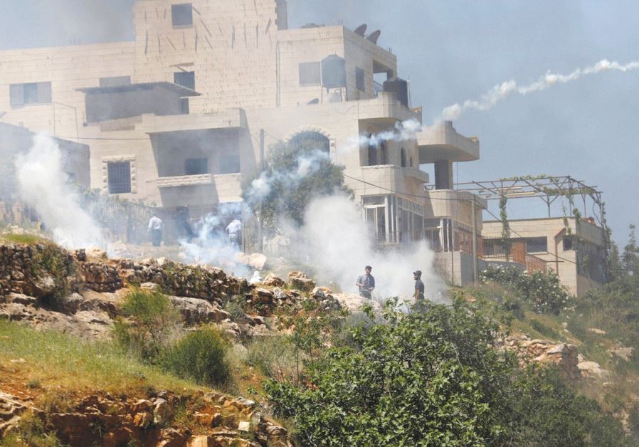 A PALESTINIAN RIOTER throws back a tear-gas cannister fired by IDF troops near Ofer Prison