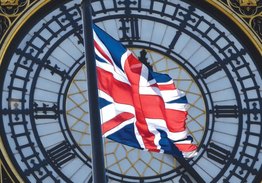 A Union Jack flag flies in front of the clock face on the Houses of Parliament in central London