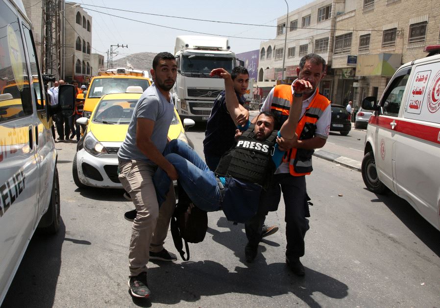 A wounded Palestinian reporter is carried by a medic and civilians on May 18, 2017 near the Hawara military checkpoint.