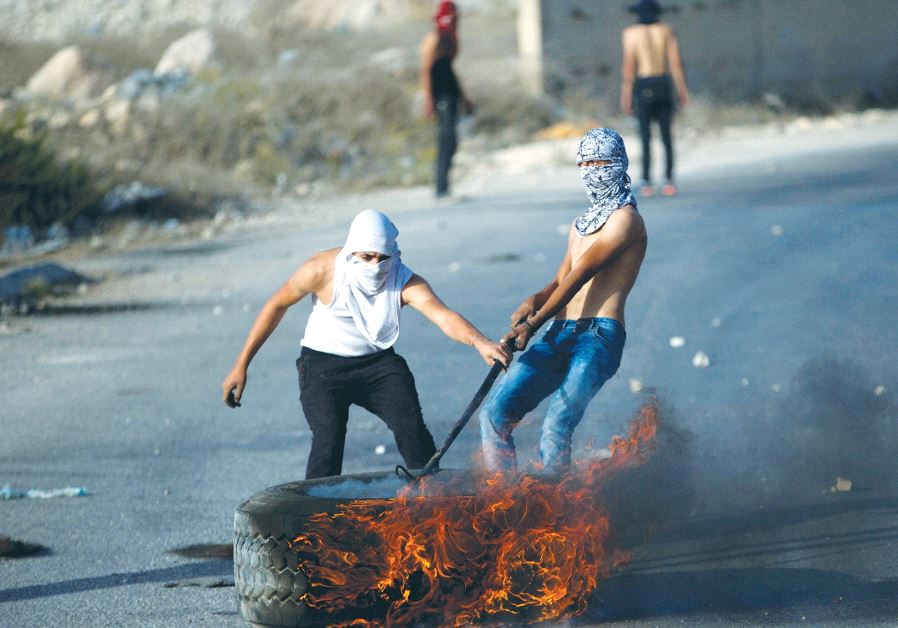 PALESTINIAN PROTESTERS drag a burning tire during a protest in a-Ram, northeast of Jerusalem.