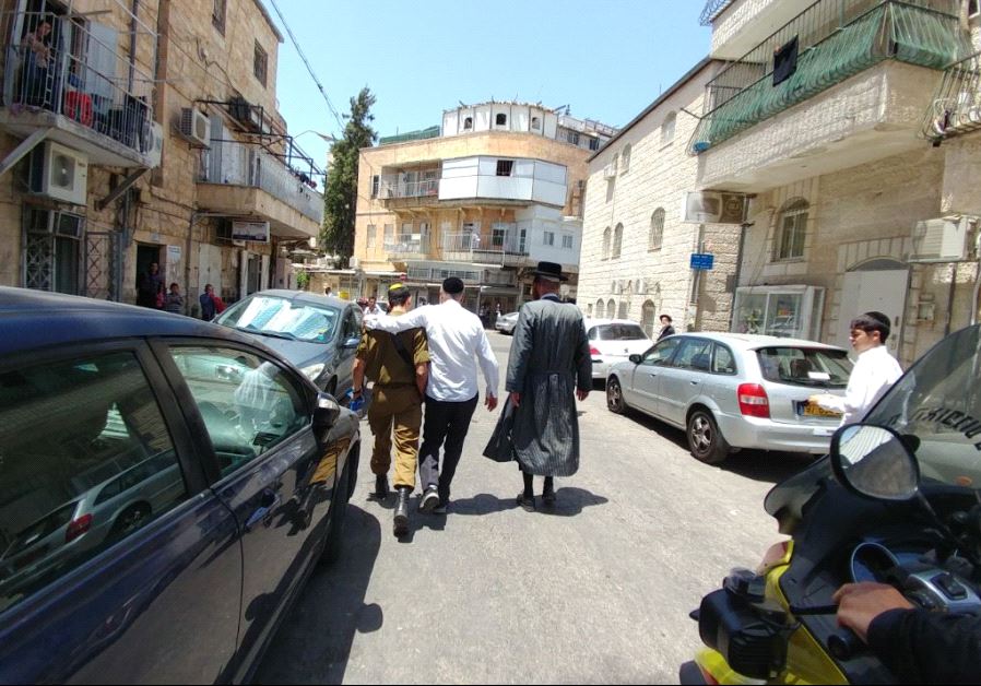 A TOLDOT AHARON Hassid (right) and another haredi man escort the son of former MK Dov Lipman, who is a soldier, away from an anti-Zionist mob in the capital’s Mea She’arim neighborhood on Friday.
