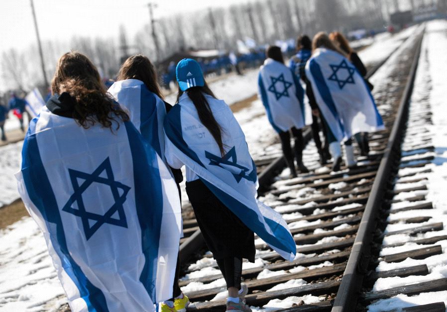 People wear Israeli flags around their shoulders as they walk on the railroad tracks inside the former Nazi death camp of Birkenau (Auschwitz II) in Oswiecim-Brzezinka, southern Poland April 8, 2013.