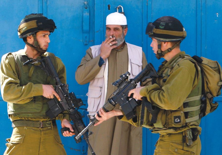 A Palestinian man smokes a cigarette beside Israeli soldiers after minor clashes with Palestinian stone-throwers in the West Bank city of Hebron February 23, 2010